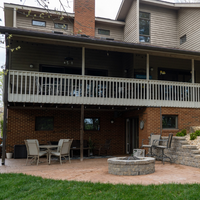 Under Deck Roof Systems walk out patio with seating, fire pit and stone retaining wall attached to a house