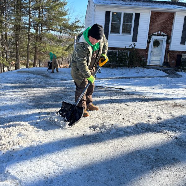 Workers shoveling snow and ice from a residential driveway on a sunny winter day, ensuring safe access to the home.