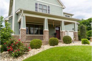 Beautiful suburban home with a well-maintained front yard, vibrant landscaping featuring neatly trimmed shrubs, red flowers, and decorative stone beds.