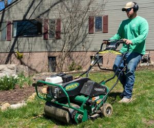 Landscaping professional operating a Ryan Lawnaire V aerator on a residential lawn to improve soil health and grass growth.